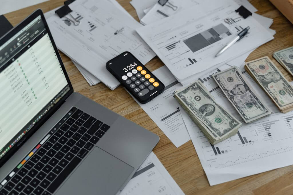 a phone, a computer, and some piles of money lined up together.